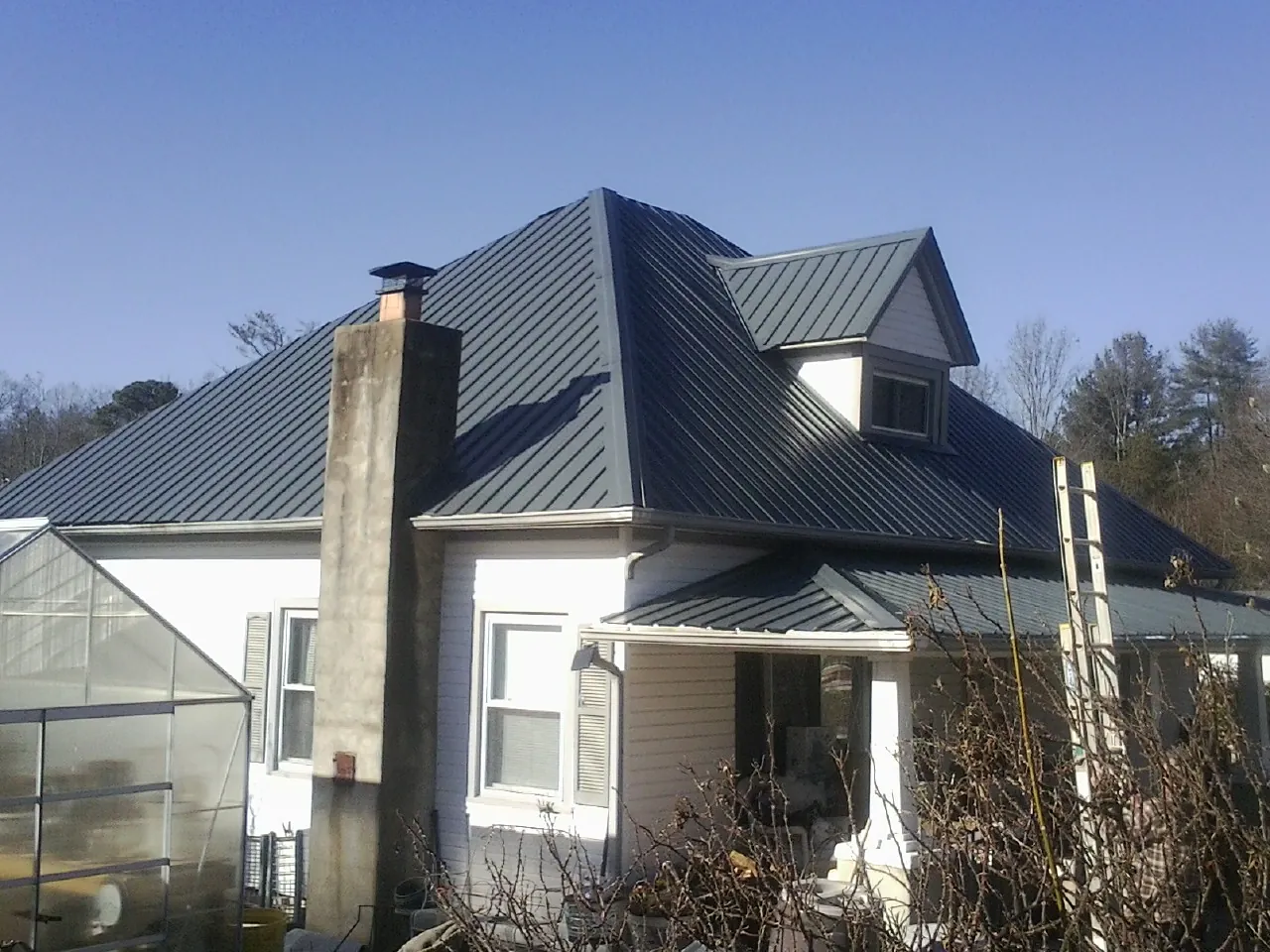 Dark blue standing seam metal roof on a white farmhouse with dormer — Slate & Tile Roof Repair by Roofing Brothers in Yulee