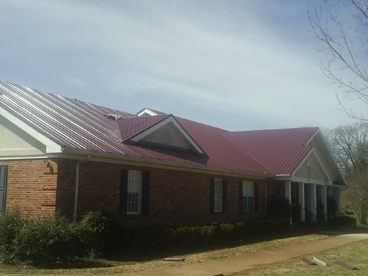 Red metal roof with gabled entries on a long brick building, from a Hail Damage Roof Repair job in Yulee
