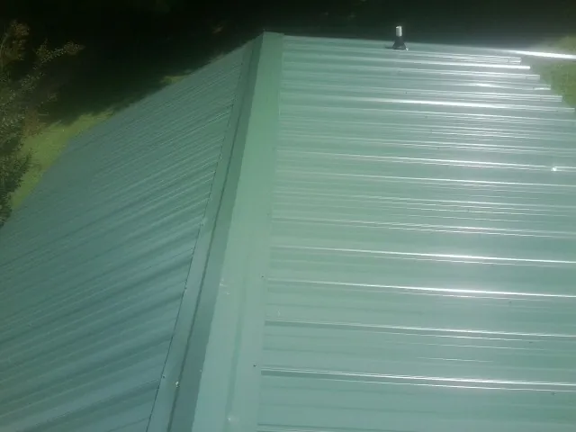 New green metal panels meeting at the ridge of a roof — Flat Roof Repair work by our crew in Yulee