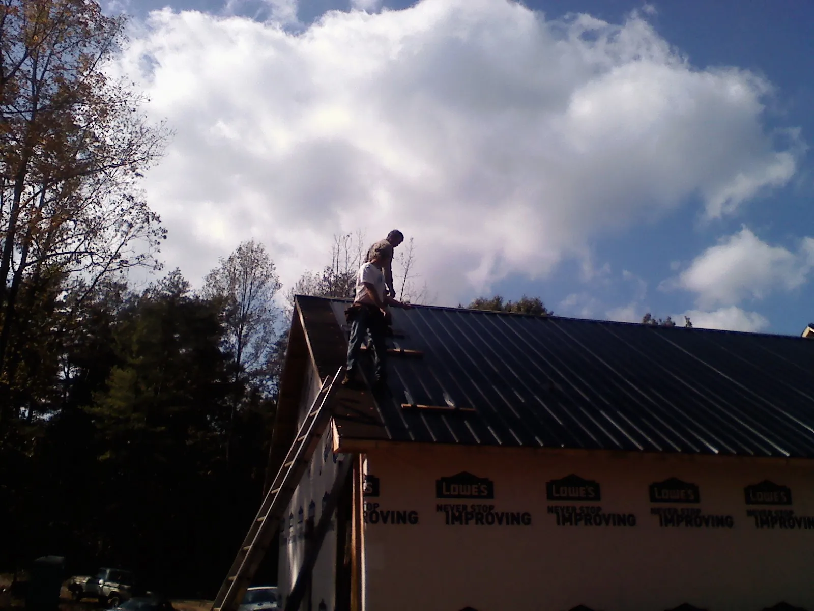 Roofer fastening dark metal panels high against a cloudy sky, from a Roof Inspection job in Yulee