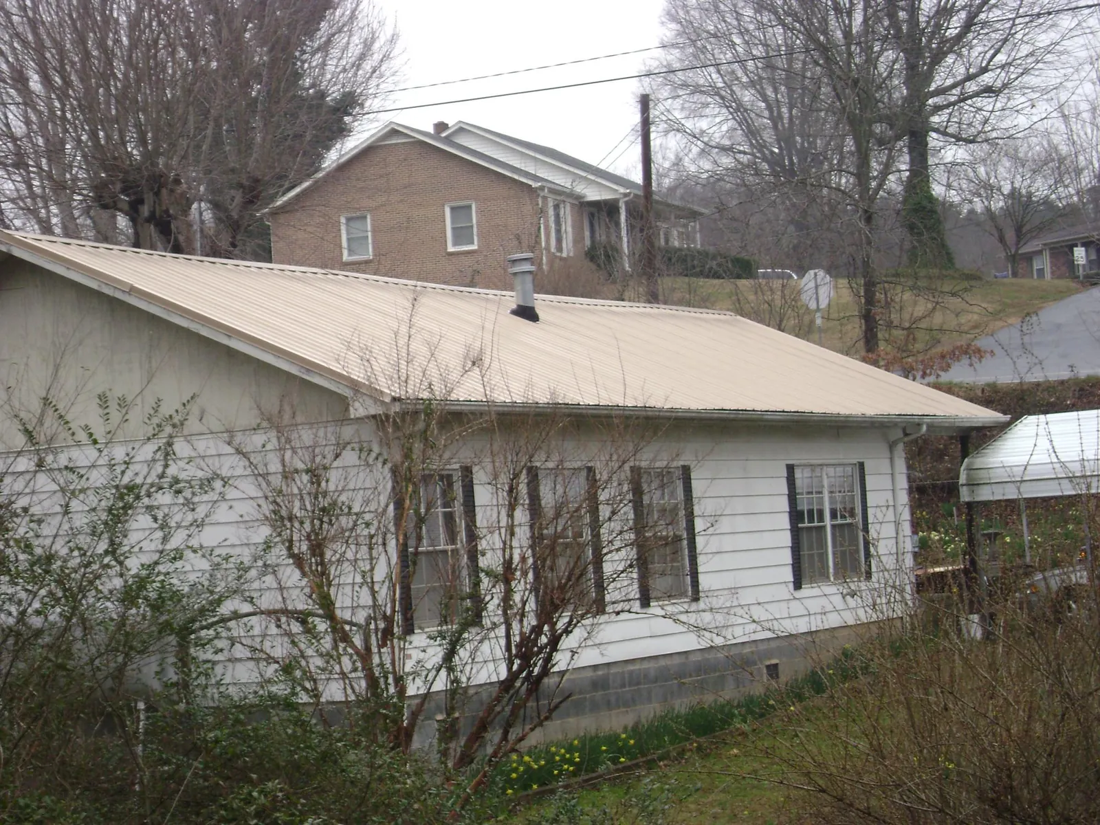 Tan metal roof on a white sided house set into a hillside — Commercial Roofing by Roofing Brothers in Yulee